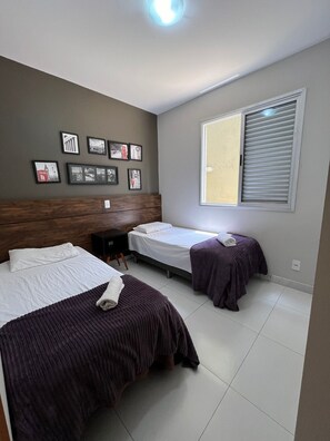 A hotel room with two beds, a desk, and a window with blinds.