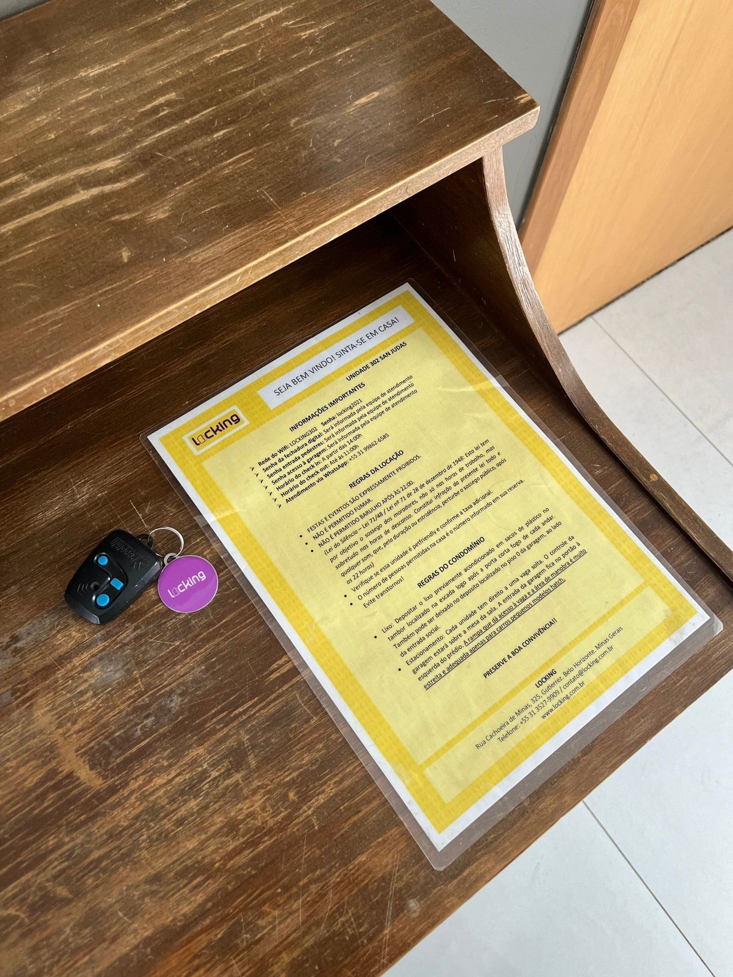 Eine gelbe Informationskarte auf einem Holztisch, zusammen mit einem Schlüsselanhänger und einer Fernbedienung.