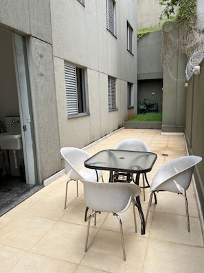 A small outdoor patio with a table and four chairs, a sink, and a window with blinds.