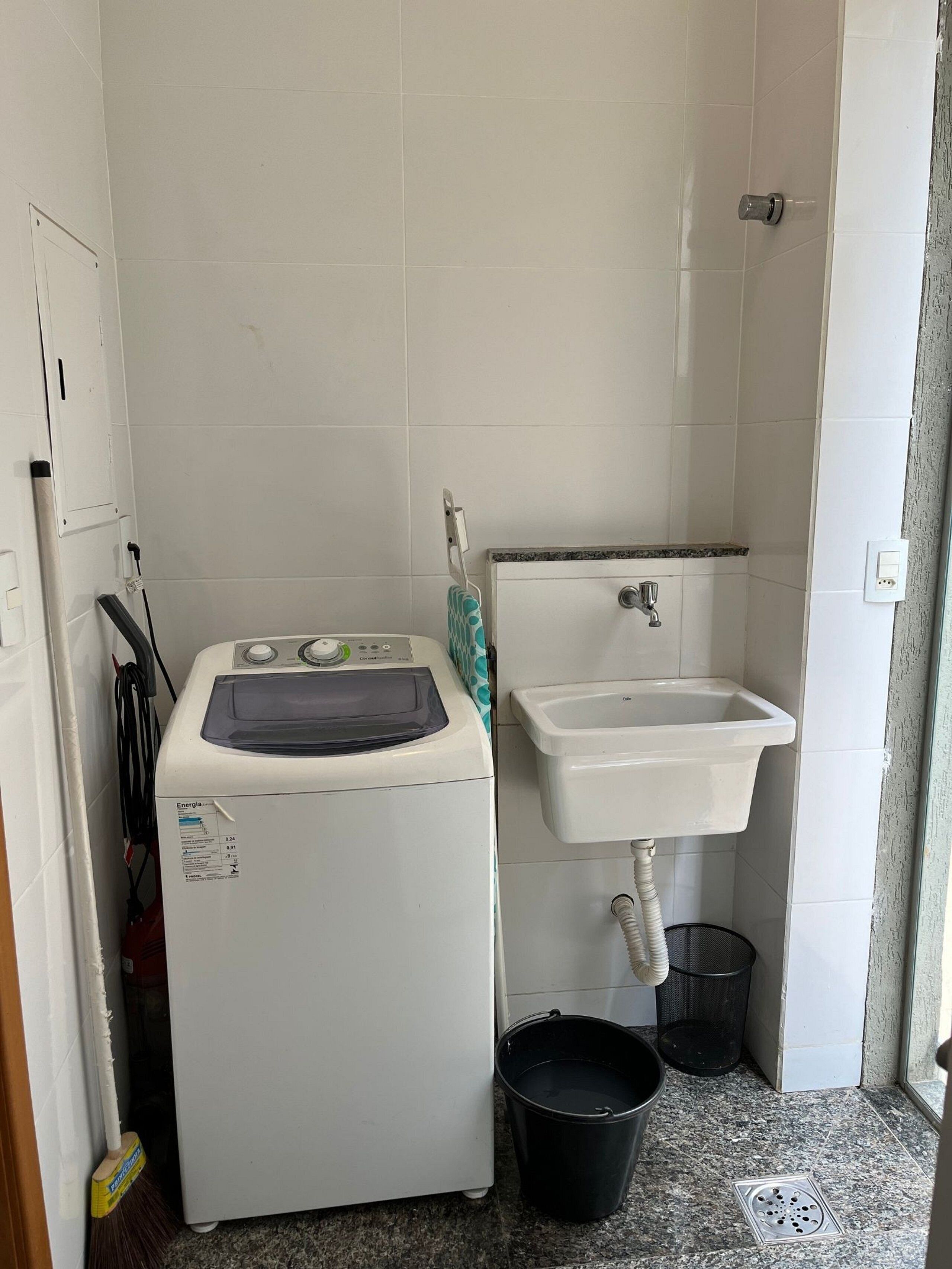 A laundry area with a washing machine, a sink, and a bucket.