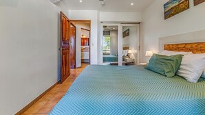 Une chambre à coucher comprenant un lit, un ventilateur de plafond, une table de chevet et une porte donnant sur une autre pièce.