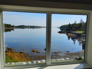 A view through a window of a calm lake with a dock, rocky shore, and forested area.