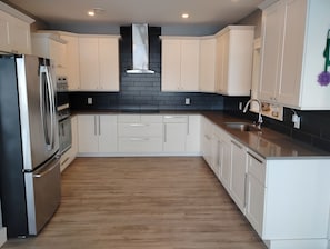 A modern kitchen with white cabinets, a stainless steel refrigerator, and a black backsplash.