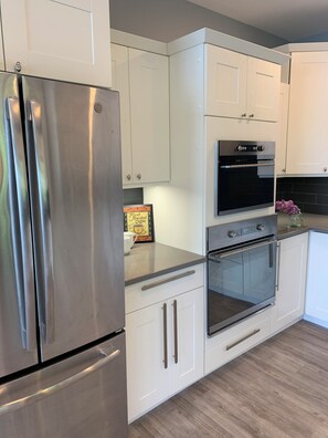 A modern kitchen with stainless steel appliances, white cabinetry, and a black tiled backsplash.