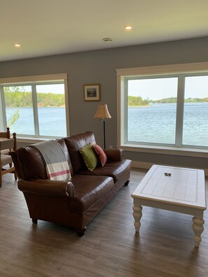 A living room with a leather sofa, a white coffee table, and large windows overlooking a body of water.
