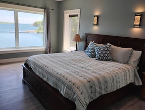 A bedroom with a large bed, a view of the water, and two wall-mounted lights. - Oceanfront Kayaking retreat close to Lunenburg (Lunenburg)
