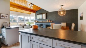 Une cuisine moderne dotée d’un grand îlot central, d’une cheminée et d’un coin repas offrant une vue sur l’extérieur.