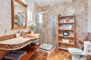 A bathroom with a curved vanity, a glass shower enclosure, a toilet, and a shelf with toiletries.