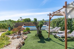 Um quintal com piscina, cadeiras de descanso e um pergolado.