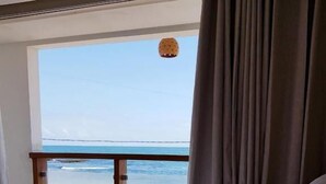 A bedroom with a view of the beach, a bed with pillows, and a hanging light fixture. - Pousada Manhã Dourada (Morro de São Paulo)