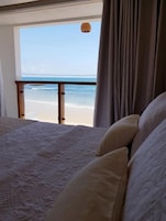 Un dormitorio con vista a la playa, una cama con almohadas y una lámpara colgante.