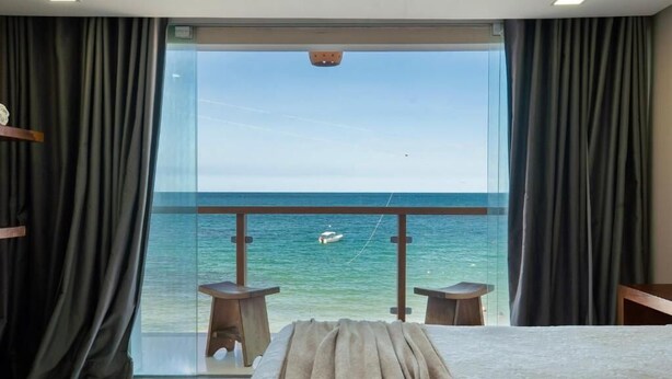 A bedroom with a large bed, two small tables, and a view of the sea through a glass door. - Pousada Manhã Dourada (Morro de São Paulo)