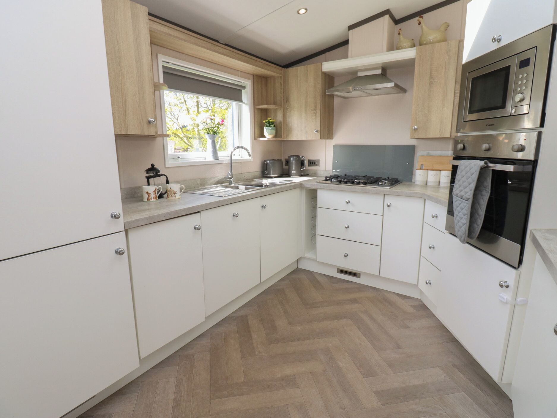 A modern kitchen with white cabinets, a stainless steel oven, a microwave, and a window with plants.