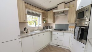 A modern kitchen with white cabinets, a stainless steel oven, a microwave, and a window with plants. - 52 Parkview, Badger's Retreat (Richmond)
