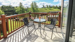 A balcony with a wooden railing, two chairs, a small round table, and a bottle of wine.