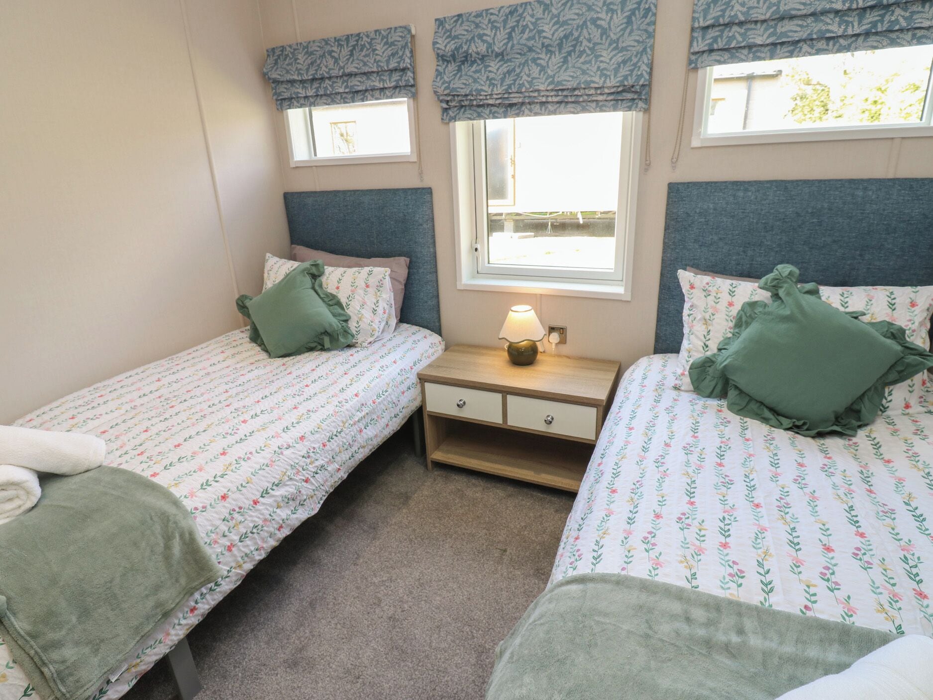 A bedroom with two single beds, a bedside table with a lamp, and a window with a view.