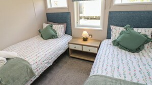 A bedroom with two single beds, a bedside table with a lamp, and a window with a view. - 52 Parkview, Badger's Retreat (Richmond)