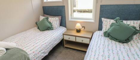 A bedroom with two single beds, a bedside table with a lamp, and a window with a view.