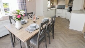 A modern kitchen with white cabinets, a dining area with a wooden table set for four, and a view of a garden through the window. - 52 Parkview, Badger's Retreat (Richmond)
