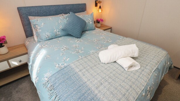 A neatly made bed with floral bedding, a blue throw blanket, and a folded towel on the side.
