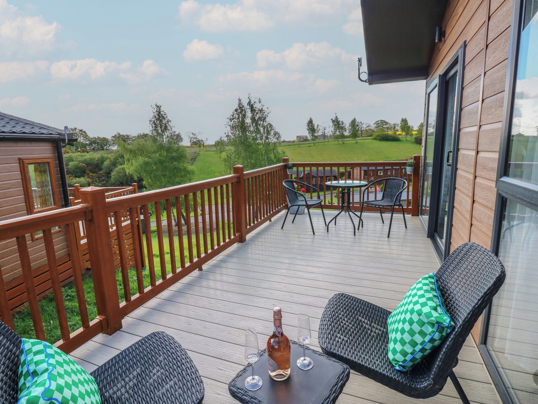 Um terraço com mobiliário exterior, uma garrafa de vinho e um copo sobre uma mesa.