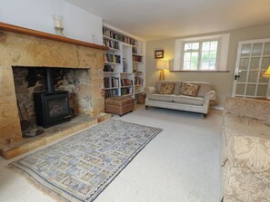 A cozy living room with a fireplace, bookshelves, a sofa, and a patterned rug. - Crantock (Sherborne)
