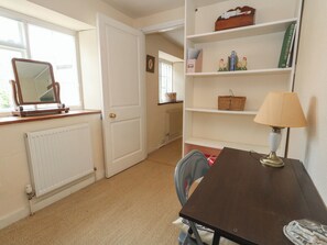 Ein Zimmer mit Heizkörper, Tür, Spiegel, Tisch mit Lampe, Stuhl und Bücherregal mit Büchern und Dekoration.
