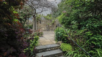 A stone staircase leading up to a stone wall, surrounded by lush greenery and plants.