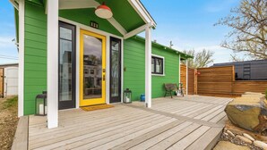 Ett grönt hus med en gul dörr, en träveranda och en liten uteplats.