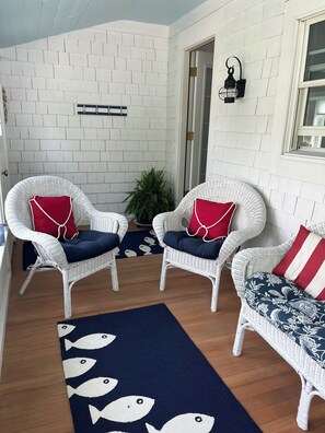 Ein Zimmer mit weißen Backsteinwänden, zwei Korbstühle mit roten und blauen Kissen, einem gemusterten Teppich und einem Fenster.