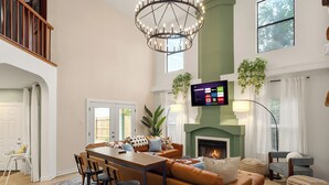 A spacious living room with a fireplace, a dining area, and a TV mounted on the wall. - The Saddle Club • Pool • Cinema • Vibes • Arcade (San Antonio)