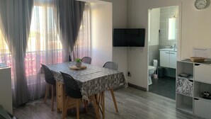 A modern room with a dining table, chairs, a TV, and a small kitchenette. - Rent studio 4 persons sea and city center (Le Grau-du-Roi)