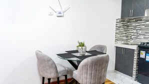 A dining area with a glass table, grey upholstered chairs, a potted plant, and a kitchen with a tiled backsplash. - Modern 1-bedroom studio apartment near downtown Cusco perfect for your stay (Cusco)