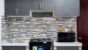 A kitchen with grey cabinets, a tiled backsplash, a gas stove, and a microwave. - Modern 1-bedroom studio apartment near downtown Cusco perfect for your stay (Cusco)