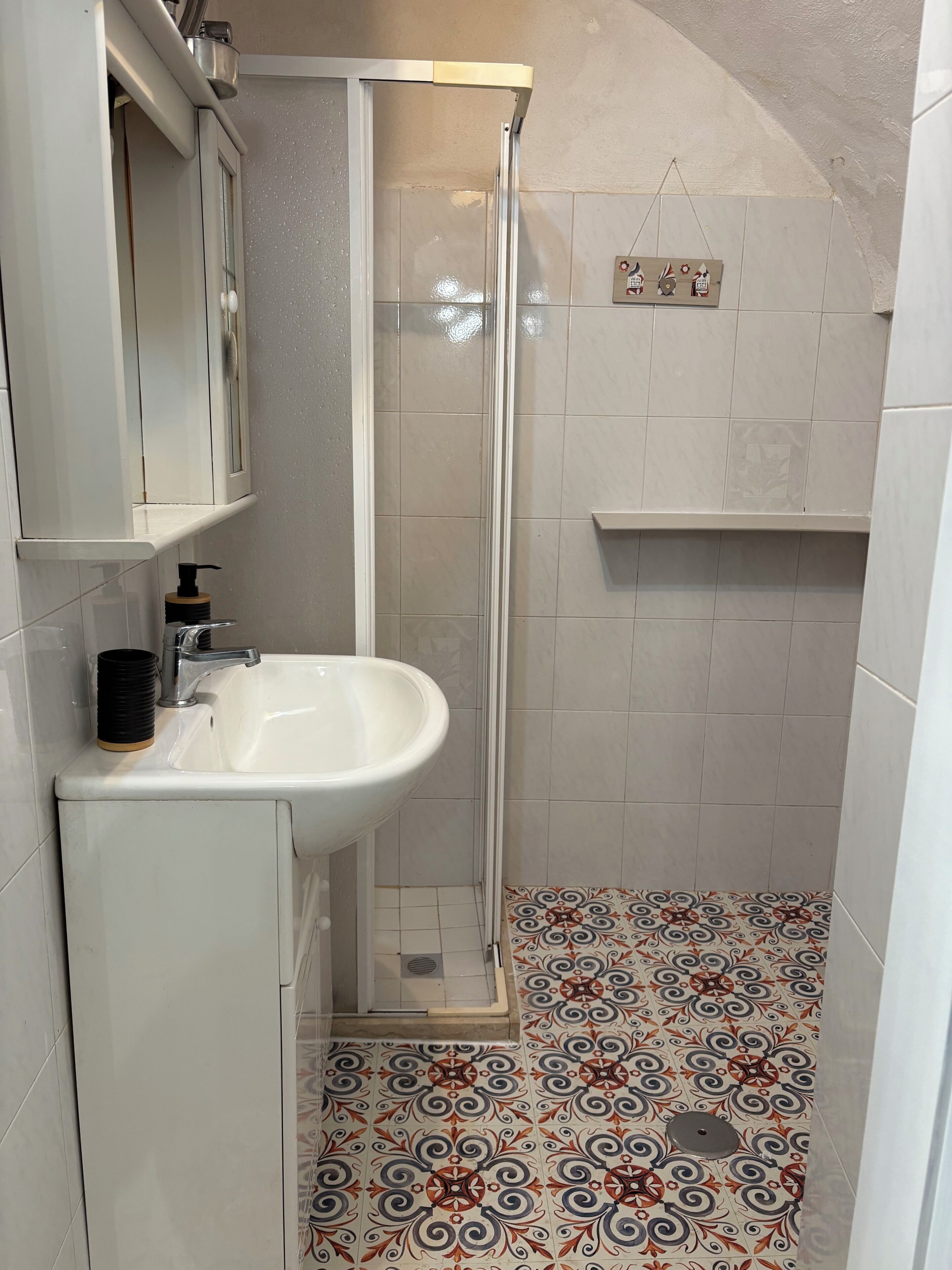 Ein Badezimmer mit einem weißen Waschbecken, einer Glasdusche und fugenlosen Bodenfliesen.