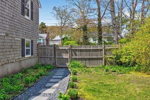 A residential backyard with a wooden fence, a gravel path, and various plants.