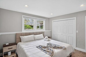 A bedroom with a bed, nightstands, a window with a view, and a door.