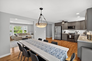 A modern kitchen with a dining area, wooden flooring, and a large window.