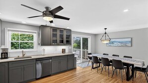 A modern kitchen with grey cabinets, a wooden countertop, a ceiling fan, and a dining area with a table and chairs. - Walk to 4 Beaches · Pool Table · Xbox · Fire Pit (Barnstable)