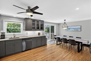 A modern kitchen with grey cabinets, a wooden countertop, a ceiling fan, and a dining area with a table and chairs.