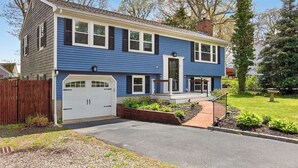 A two-story house with a garage, a front porch, and a well-maintained lawn. - Walk to 4 Beaches · Pool Table · Xbox · Fire Pit (Barnstable)