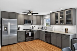 A modern kitchen with grey cabinets, stainless steel appliances, a ceiling fan, and a window providing natural light.