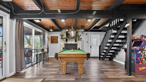 Une table de billard dans une pièce dotée de parquets en bois, d’un escalier et d’une borne d’arcade.