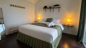 Ein Hotelzimmer mit einem großen Bett, zwei Nachttischen mit Lampen, einem Holzregal mit Pflanzen und einem Kleiderständer.