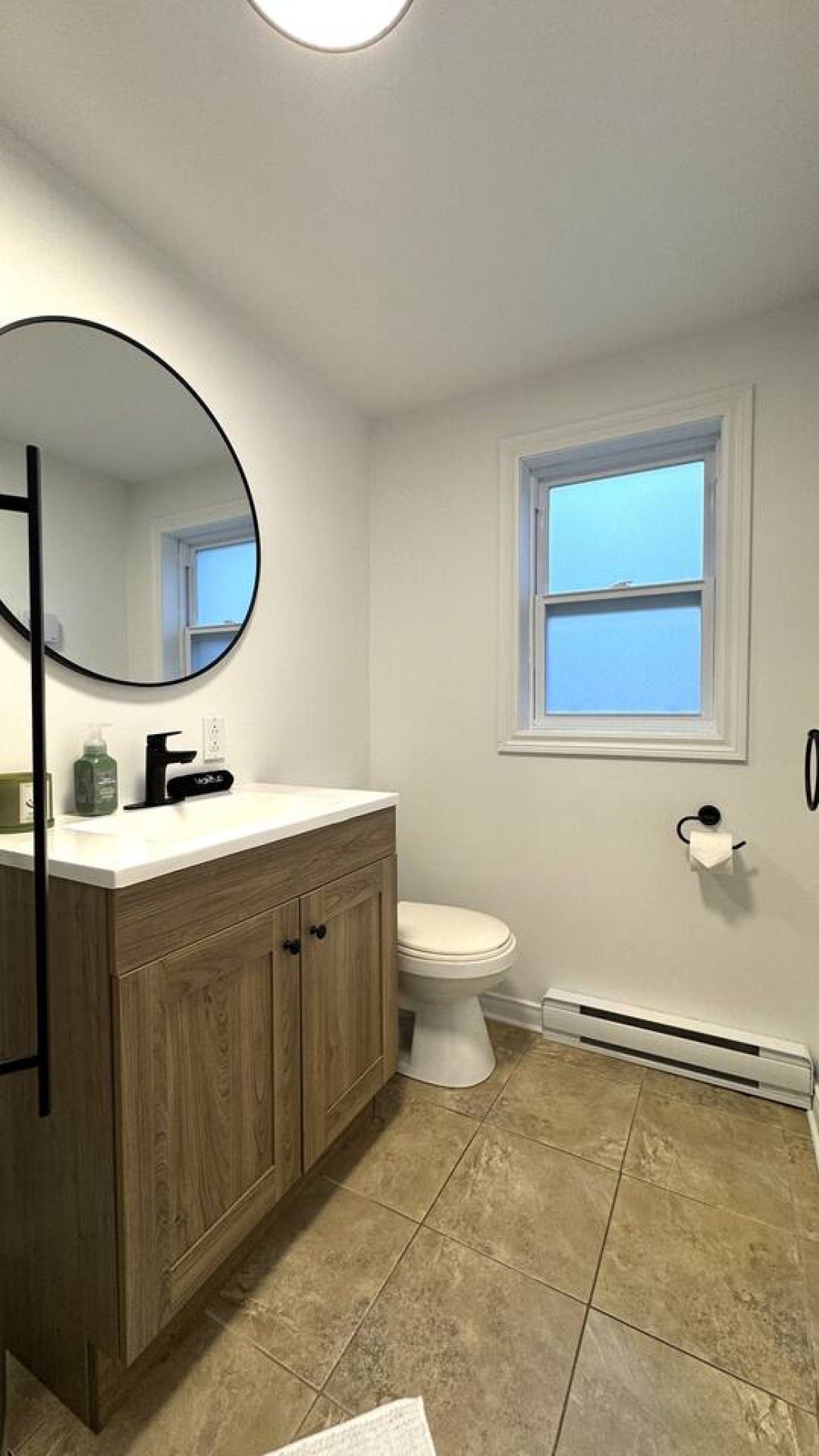 A bathroom with a toilet, a sink with a mirror, and a window.