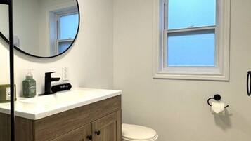 A bathroom with a toilet, a sink with a mirror, and a window.