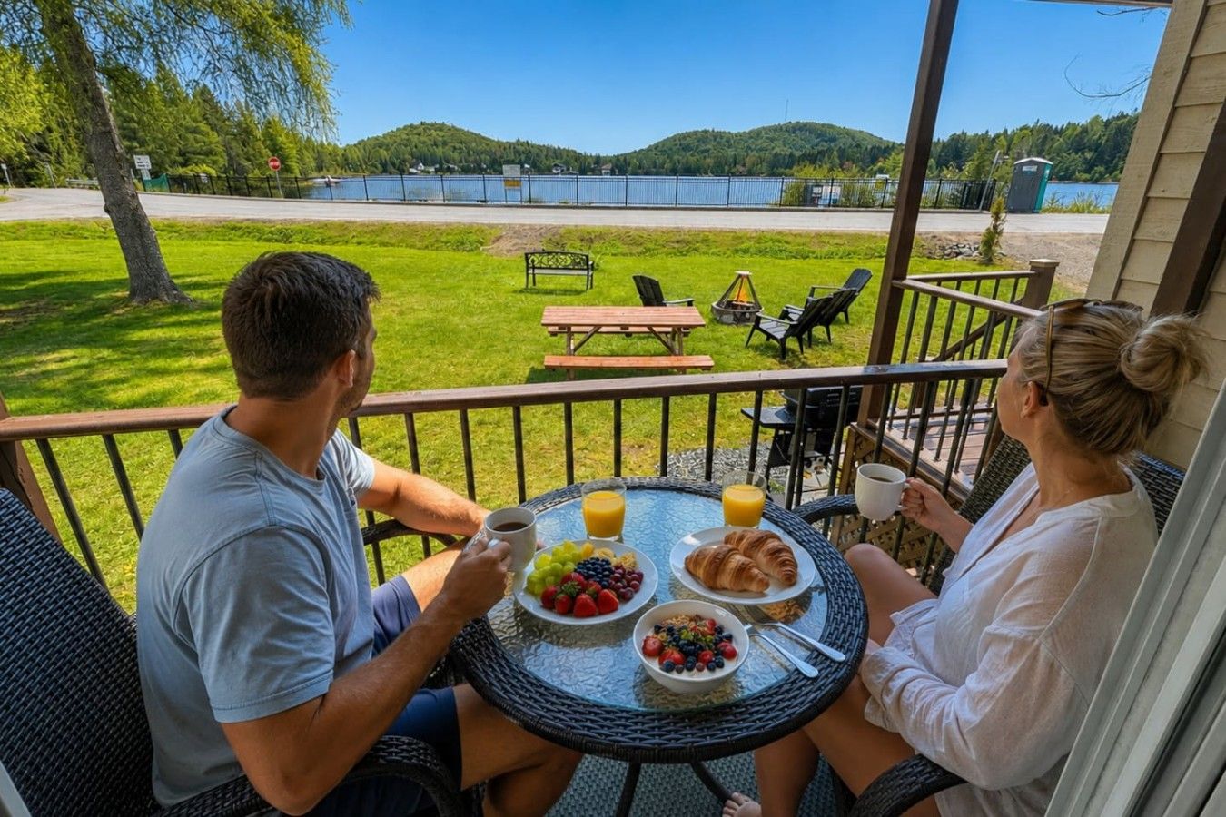 Un couple est assis à une table ronde, un petit-déjeuner devant eux, sur un balcon donnant sur un lac.