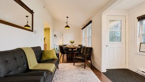 Ein Wohnzimmer mit einer Couch, einem Esstisch, Stühlen, Pendelleuchten und einer Tür zu einem weiteren Raum.