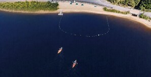 Eine Luftaufnahme einer Küstenlandschaft mit zwei Booten auf dem Wasser, einem Sandstrand und einem Gebäude mit Dach.