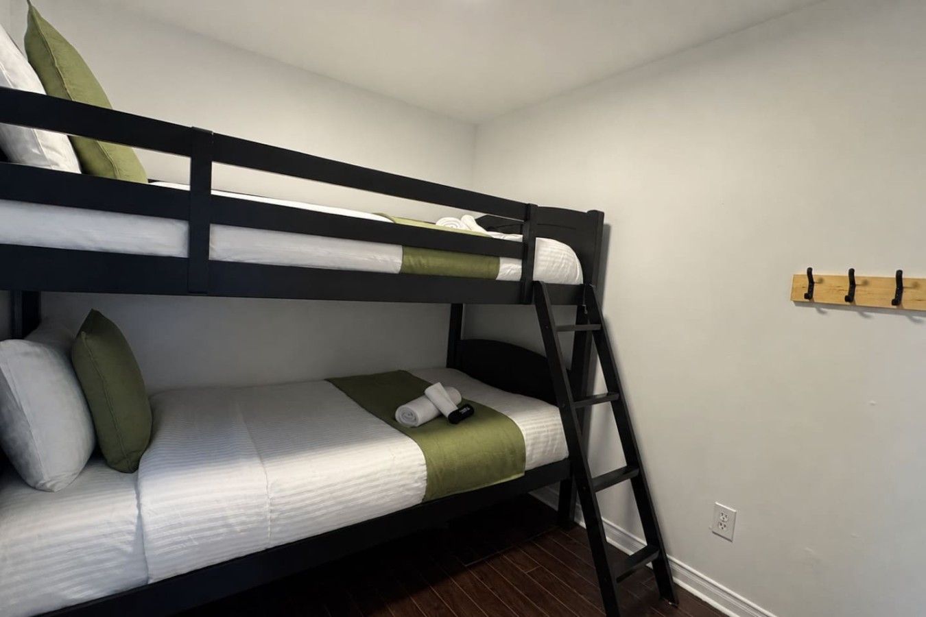 A bunk bed with a ladder, pillows, and a wooden coat rack against a plain wall.